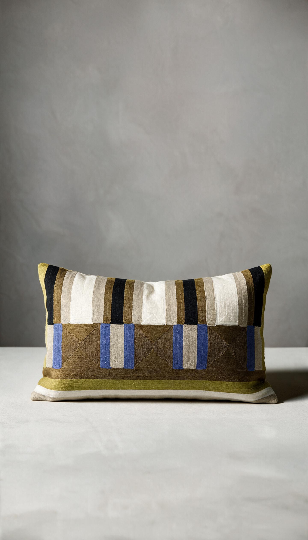 Cojín rectangular lumbar modelo Jalisco de 30x50cm, con patrón geométrico bordado a rayas y bloques combinando tonos tierra, oliva, negro, crema y detalles en azul eléctrico.