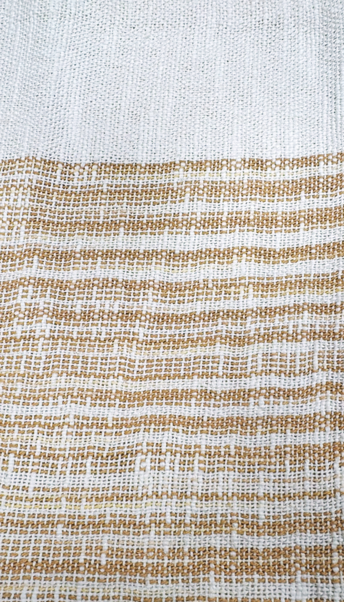 Funda de cojín rectangular modelo Amapola con diseño bicolor en tonos crudo y beige tostado, decorada con largos flecos en sus extremos laterales, sobre superficie clara.