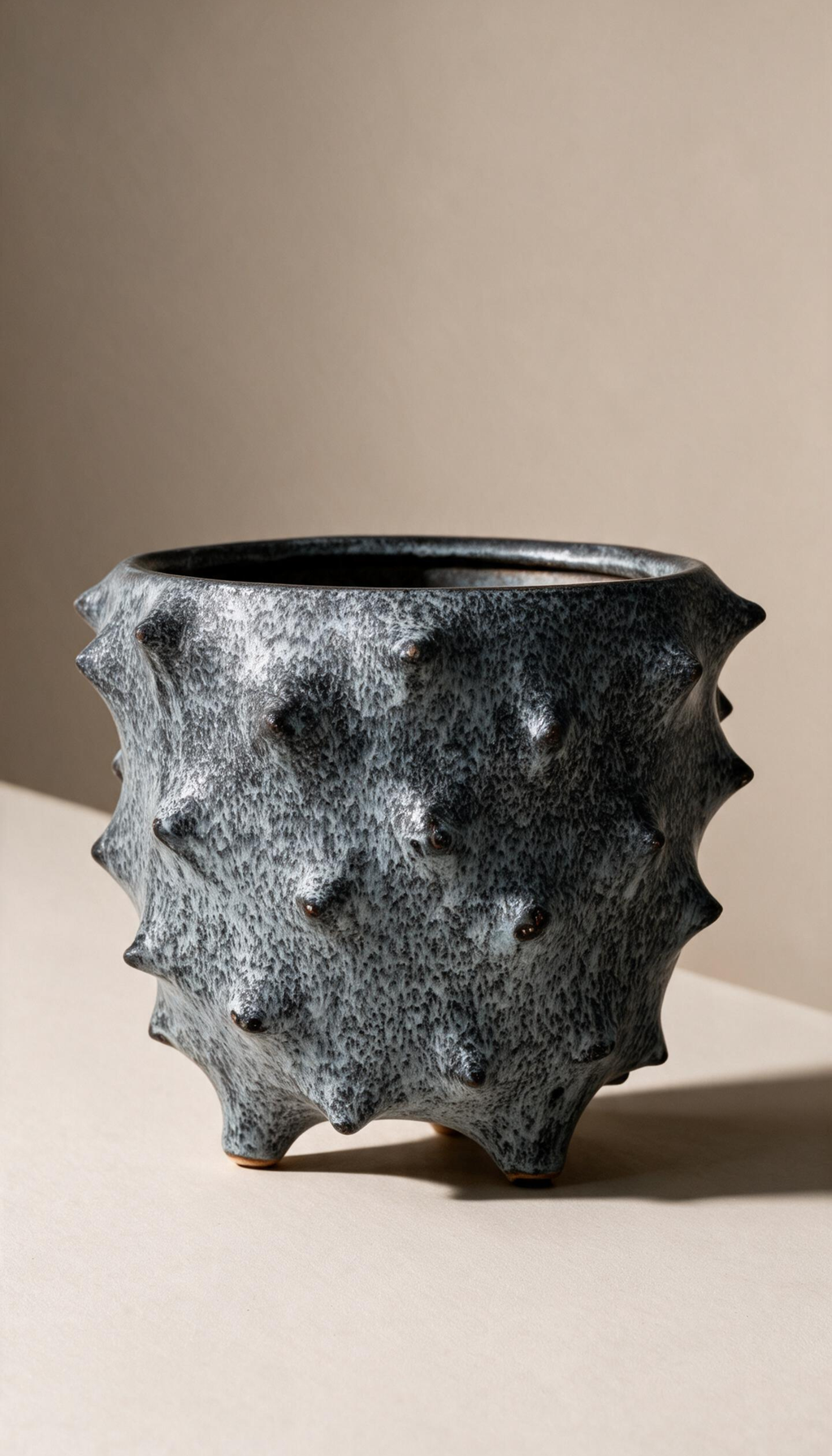 Macetero de gres modelo Brezo en color gris moteado, con diseño rústico de textura con pinchos y base con patas para plantas de interior.
