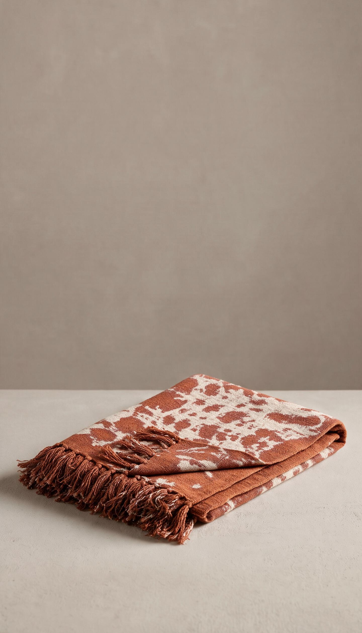 Manta de sofá modelo Salina doblada, con estampado orgánico de estilo boho en colores terracota y crema, mostrando su textura suave y acabado con flecos.