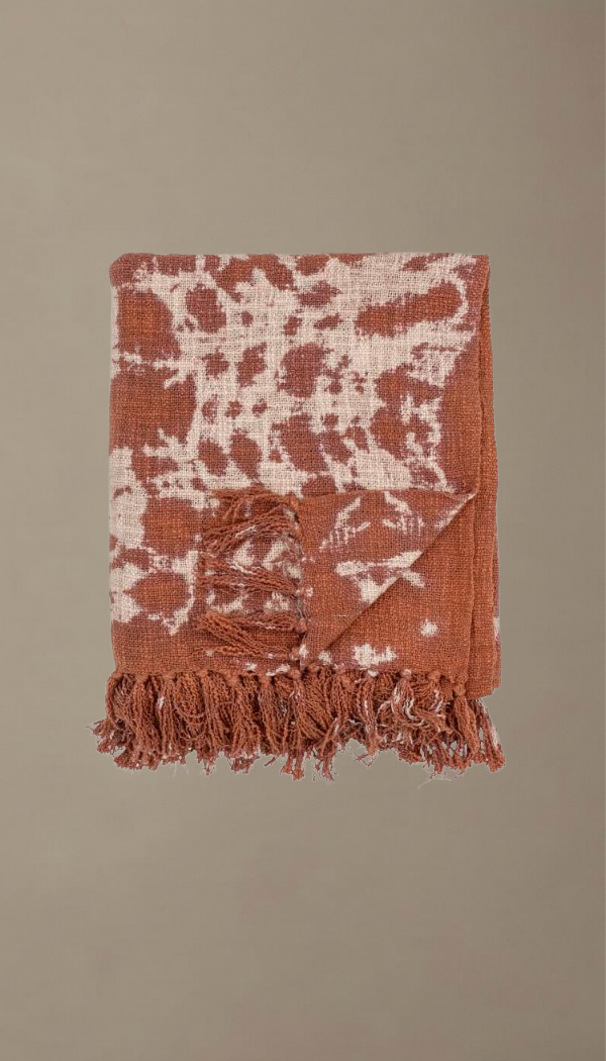 Manta de sofá modelo Salina doblada, con estampado orgánico de estilo boho en colores terracota y crema, mostrando su textura suave y acabado con flecos.