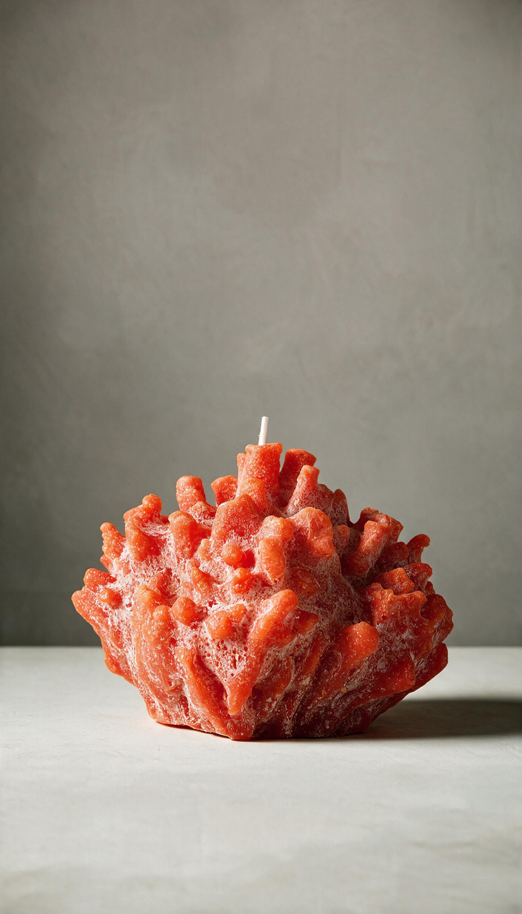 Vela decorativa escultural con forma de coral marino, mostrando una textura realista porosa en color naranja vibrante con sutiles detalles blancos empolvados.