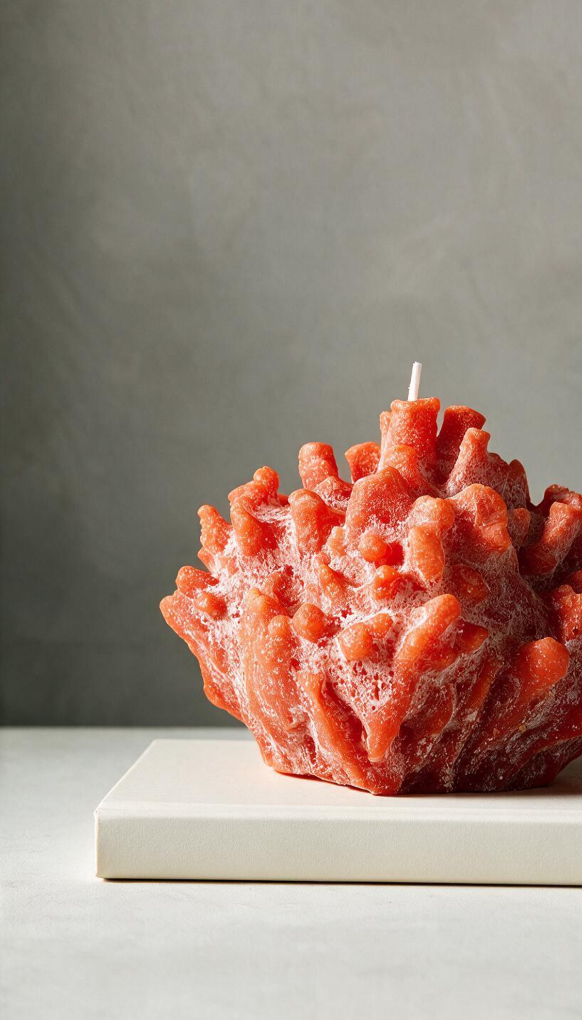 Vela decorativa escultural con forma de coral marino, mostrando una textura realista porosa en color naranja vibrante con sutiles detalles blancos empolvados.