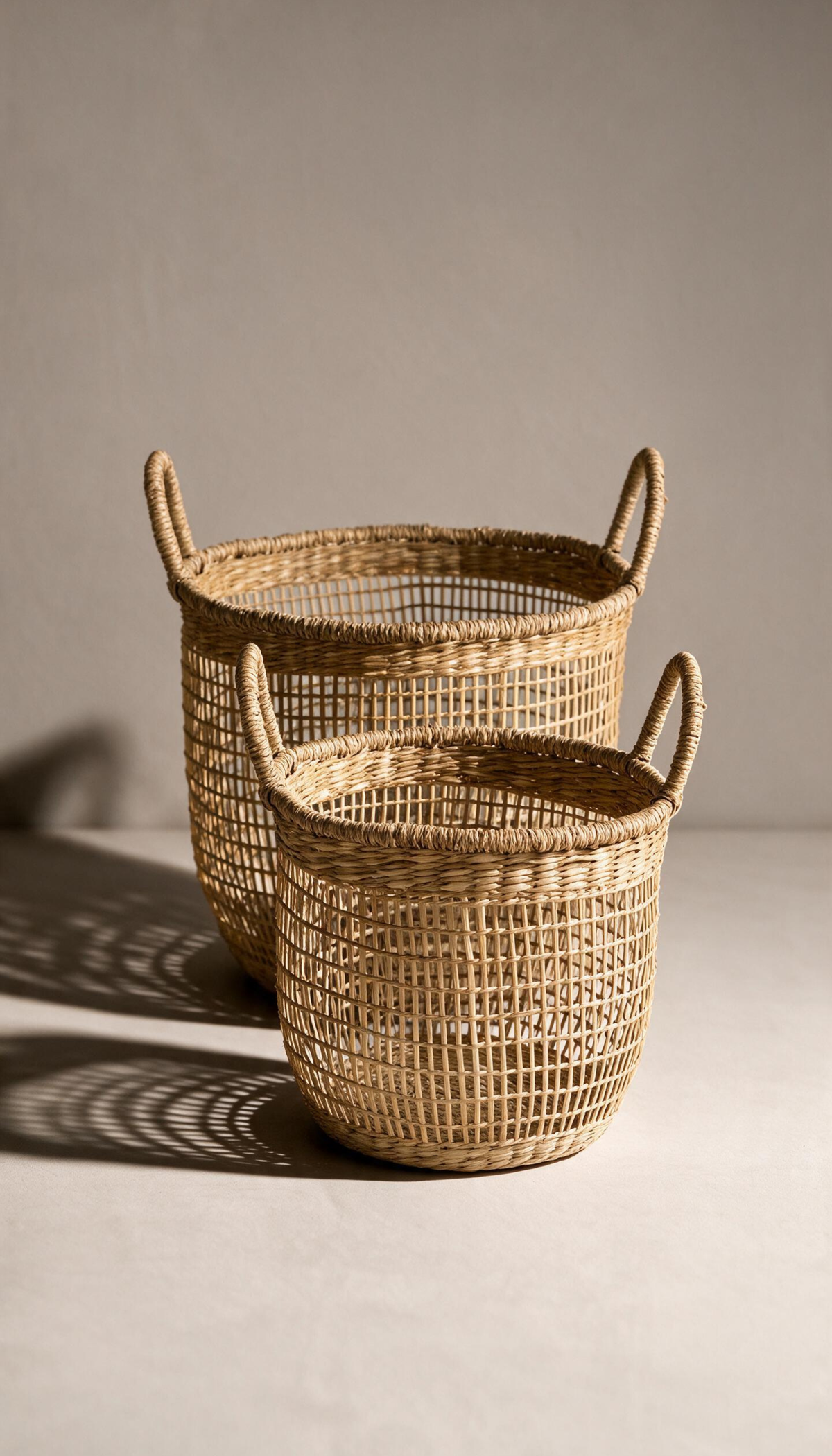 Cesta organizadora modelo Priego elaborada en fibras naturales con un diseño de trenzado abierto calado y dos asas superiores, proyectando una sombra sobre fondo neutro.
