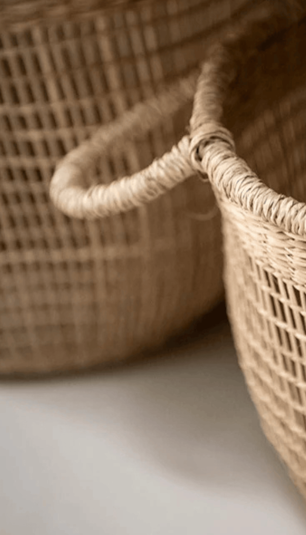 Cesta organizadora modelo Priego elaborada en fibras naturales con un diseño de trenzado abierto calado y dos asas superiores, proyectando una sombra sobre fondo neutro.