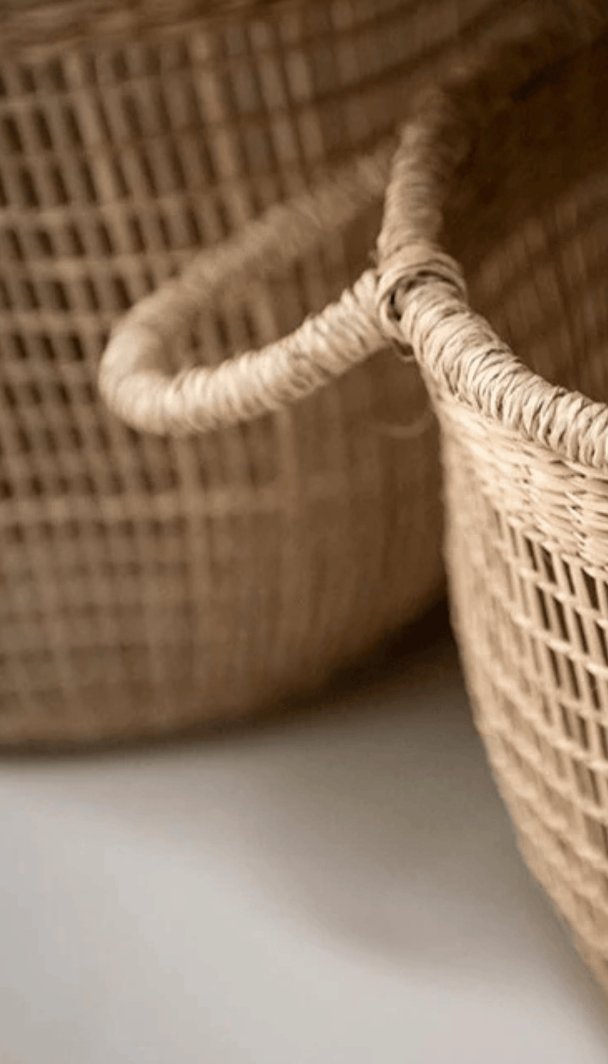 Cesta organizadora modelo Priego elaborada en fibras naturales con un diseño de trenzado abierto calado y dos asas superiores, proyectando una sombra sobre fondo neutro.